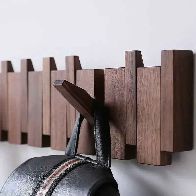 Wooden walnut coat rack on a white wall with a black bag hanging from one of them.