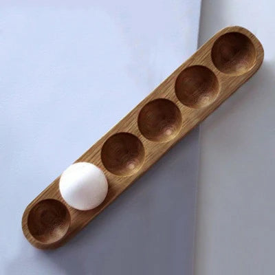 Wooden holder with six round compartments containing a single egg on a light grey background