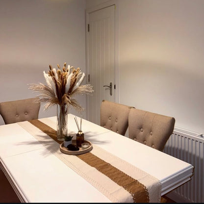 Dining table with a vase of dried pampas and decorative items, set against a neutral wall.