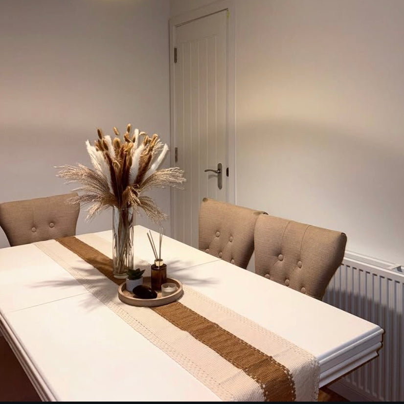 Dining table with a vase of dried pampas and decorative items, set against a neutral wall.