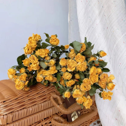 Bouquet of dried yellow roses on a wicker surface with a white textured background
