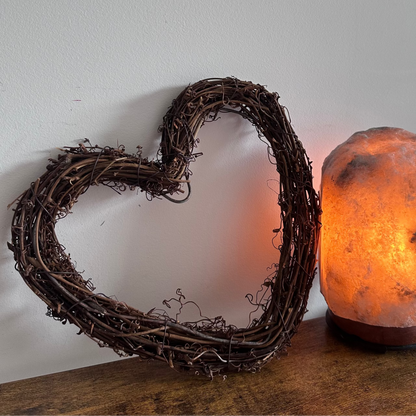Heart-shaped wreath and a salt lamp on a wooden surface with a white wall background