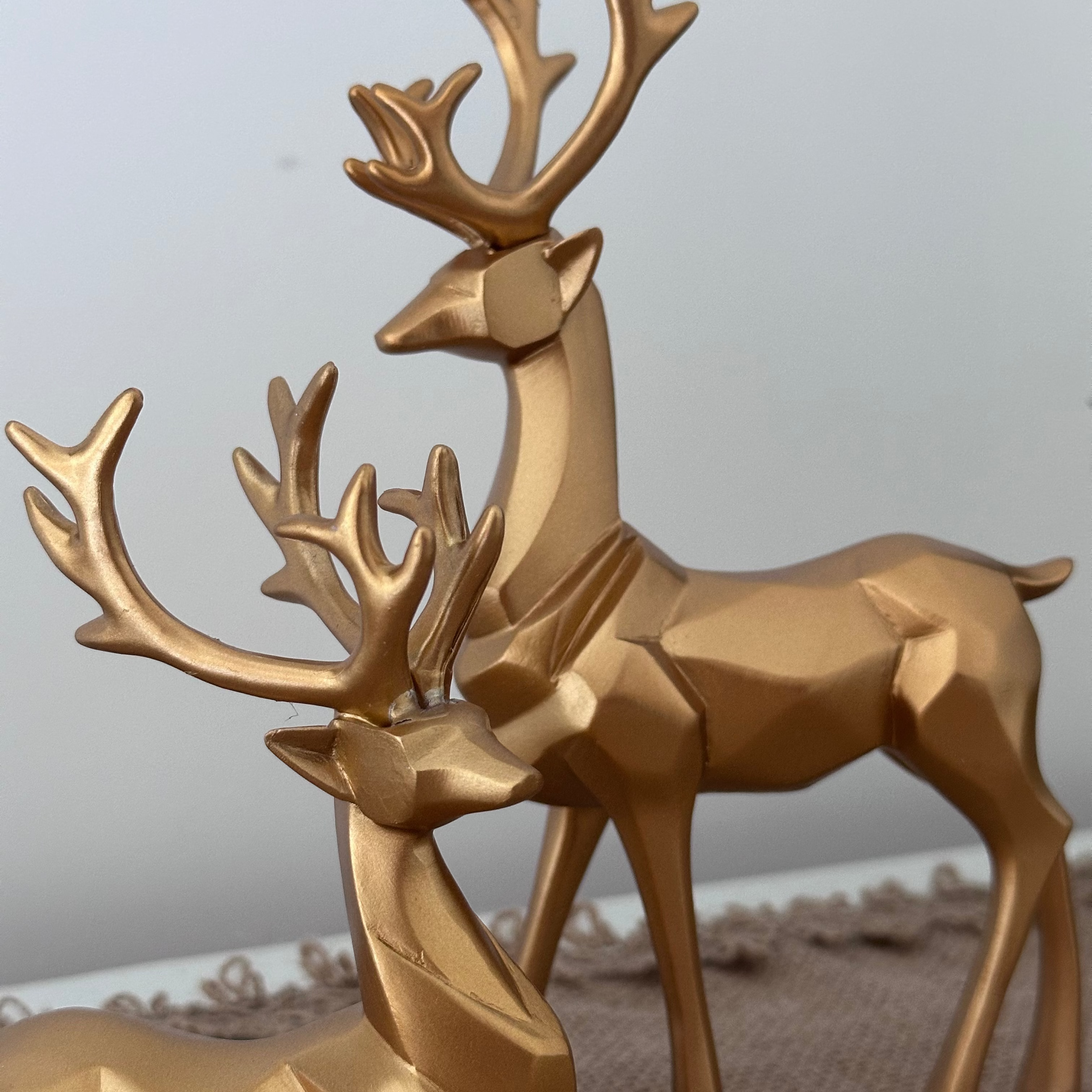 Gold deer figurines on a textured surface with a neutral background