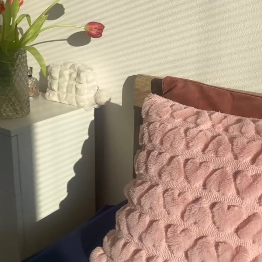 A love heart textured pillow cover displayed on a bed with tulips in the background 