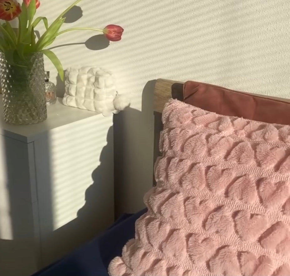 A love heart textured pillow cover displayed on a bed with tulips in the background 