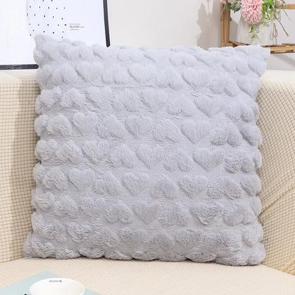 A grey plush love heart pillow cover on a couch, with a textured pattern creating a heart shape.