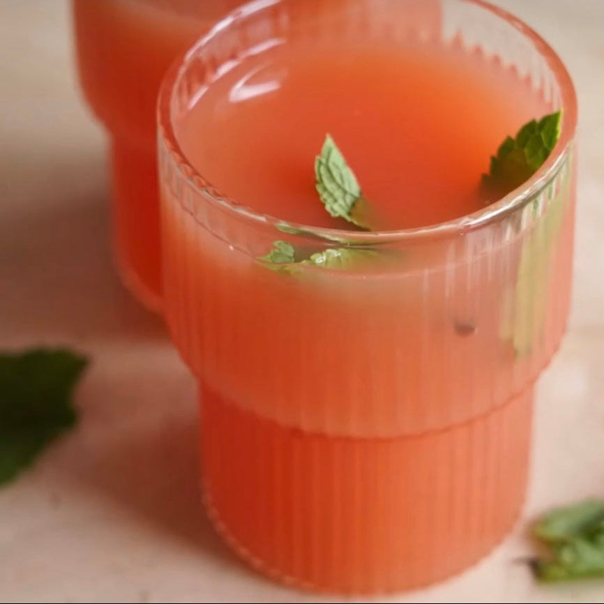 Clear glass cup with pink drink and mint leaves on a light surface