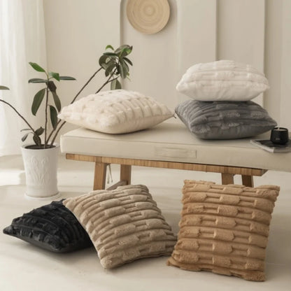 Textured pillows in various colors on a bench with a plant and cup in the background. 