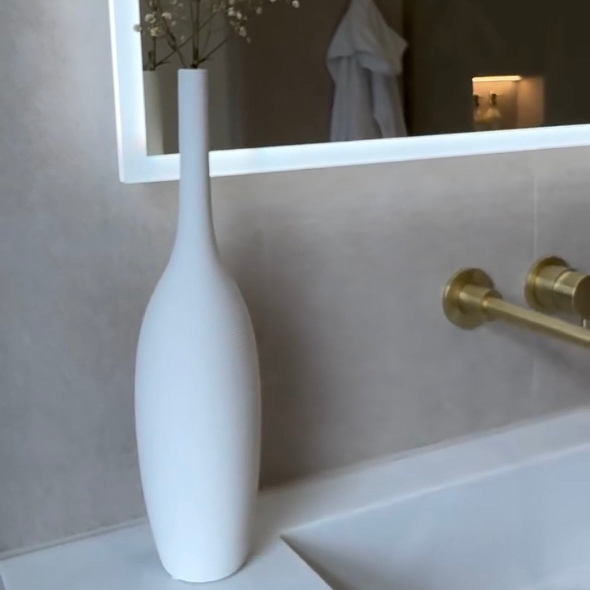 White textured vase on a bathroom counter with a mirror and towel in the background