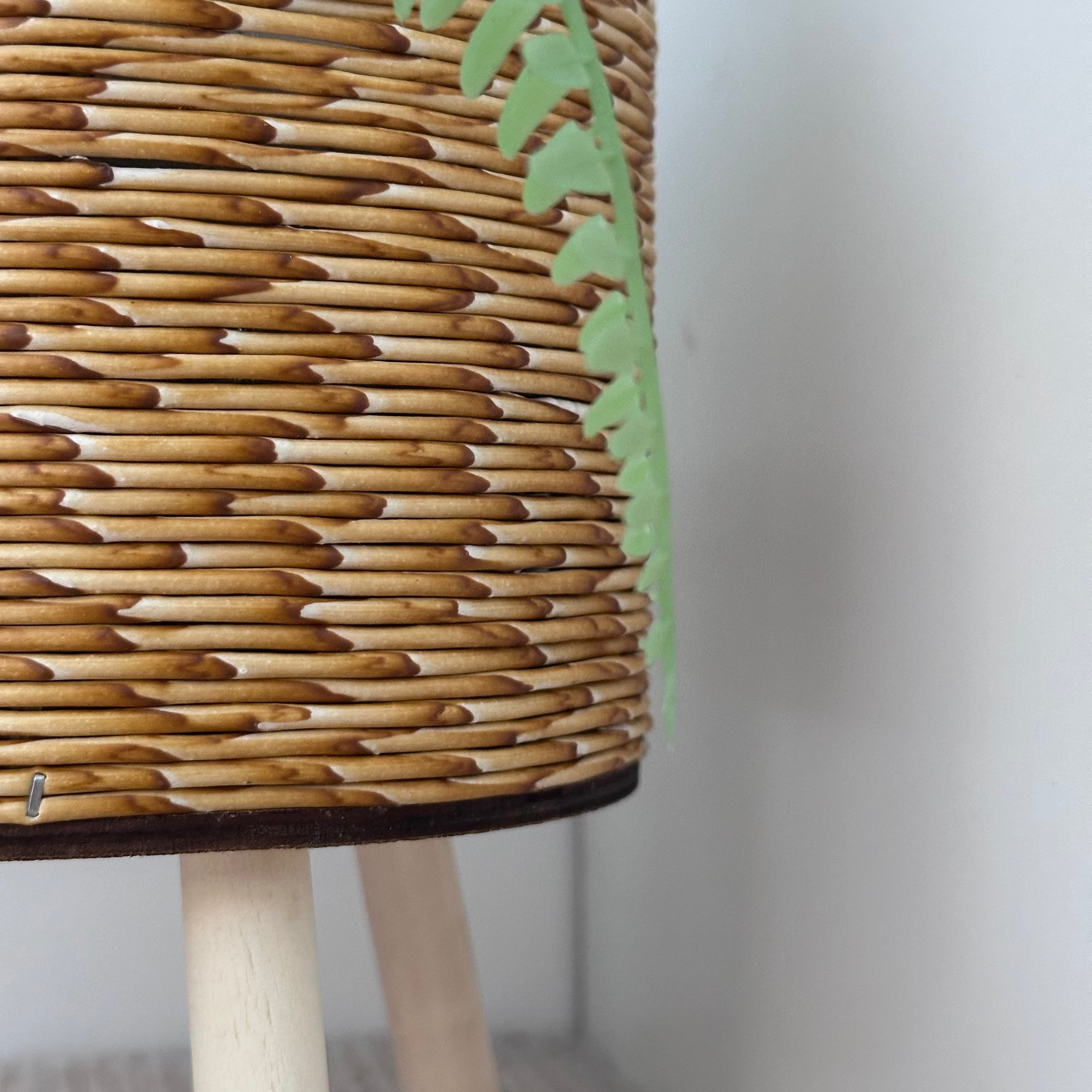Wicker stool with wooden legs and a plant on top against a white wall.