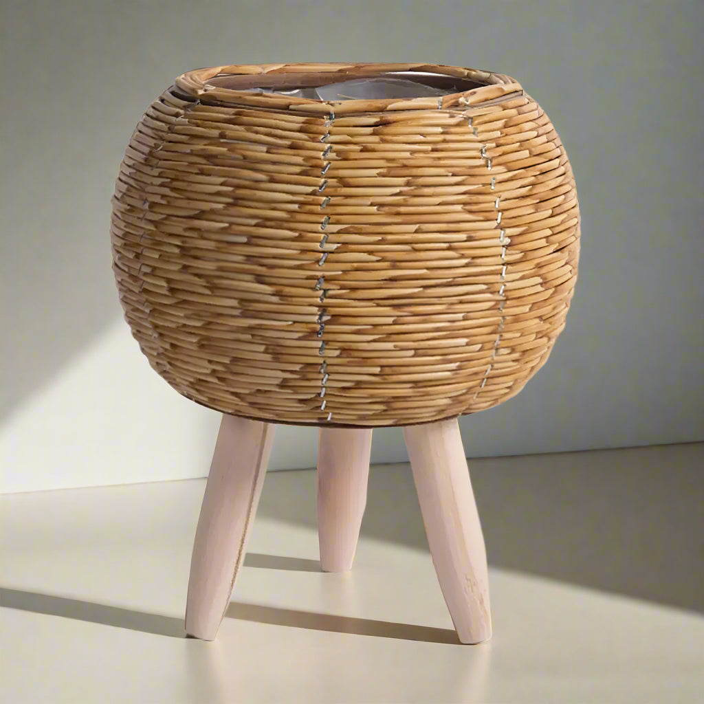 Beige rattan effect plant stand with wooden legs on a light grey background