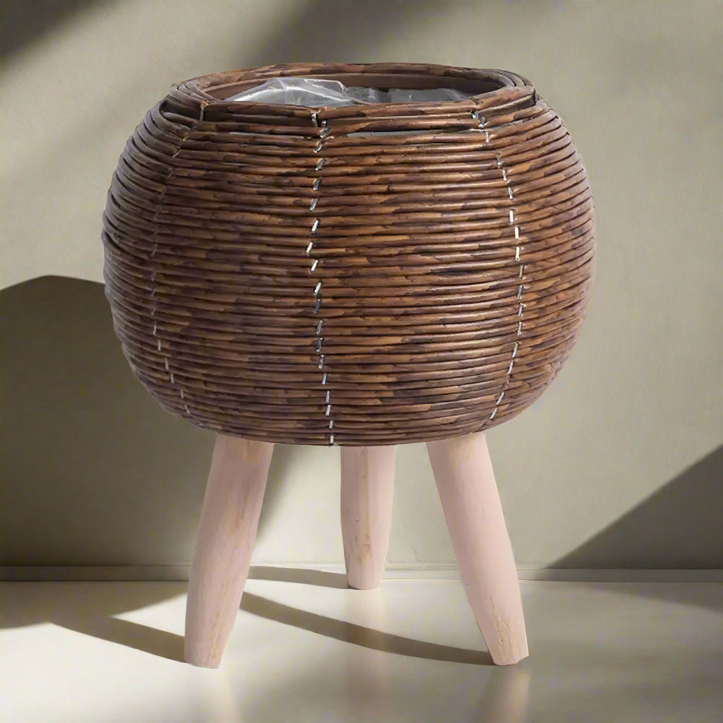 Dark brown rattan effect plant stand with wooden legs on a light grey background