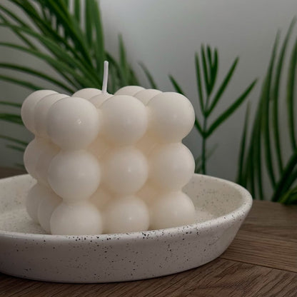 Soy wax candle with a bubble-like design on a speckled ceramic plate with plants in the background
