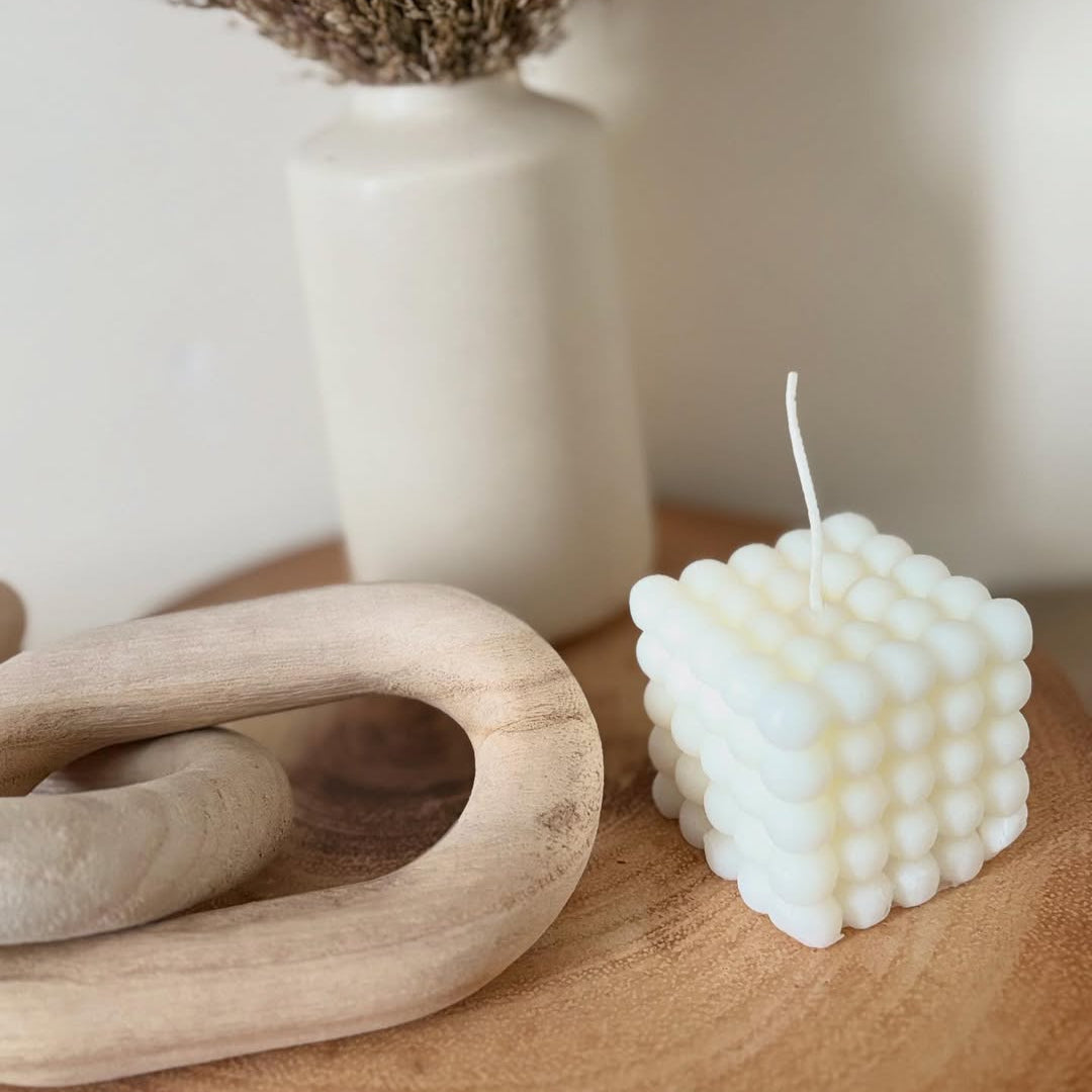 White textured candle on a wooden surface with a neutral background