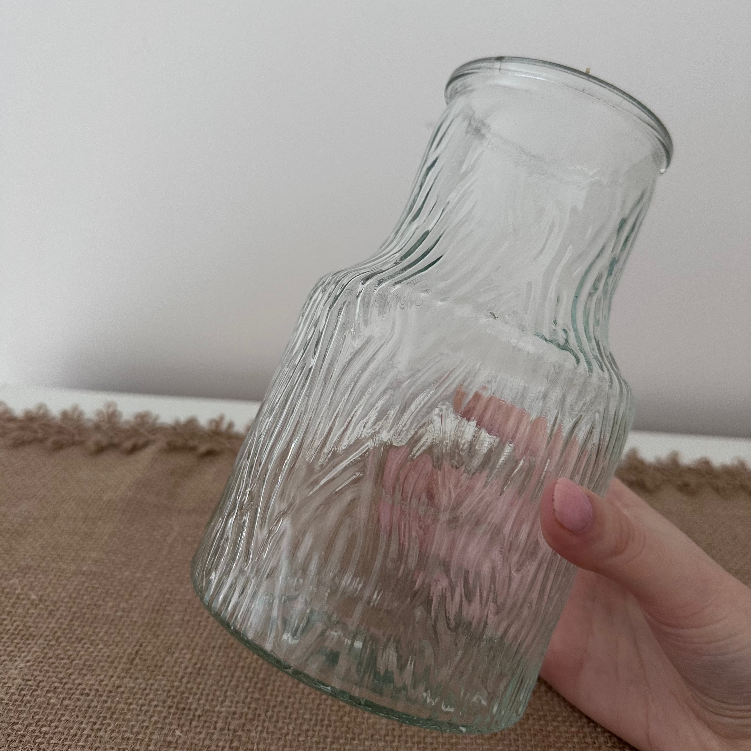 Clear glass vase held by a hand on a textured surface with a neutral background