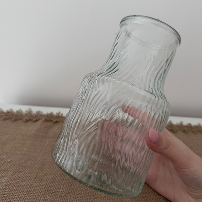 Clear glass vase held by a hand on a textured surface with a neutral background
