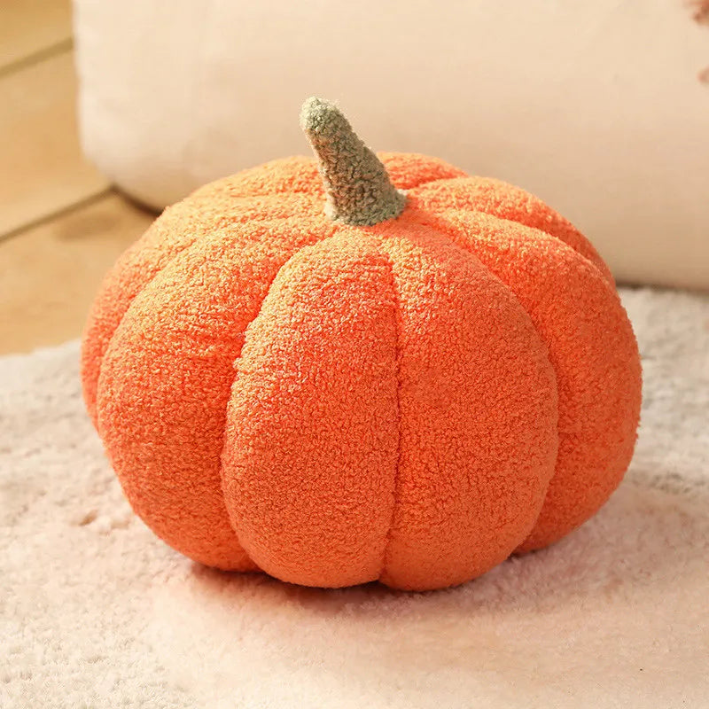 Orange textured pumpkin cushion with a green stem on a beige blanket