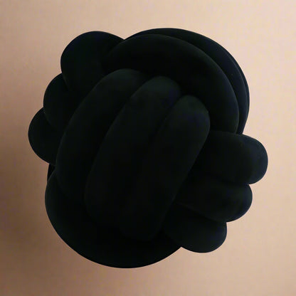 A black knot-shaped cushion against a light beige background.