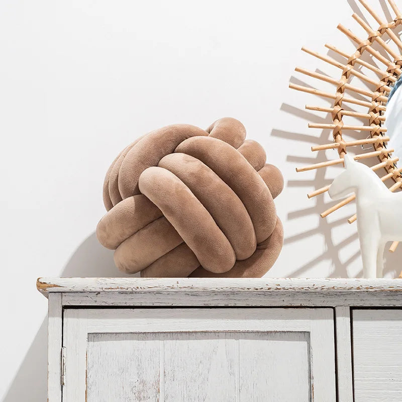 A coffee coloured knot-shaped cushion styled on a sideboard, next to an ornament.