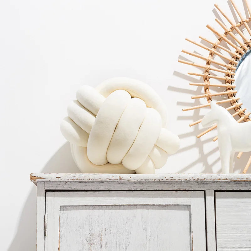 A cream-white knot-shaped cushion styled on a sideboard, next to an ornament.