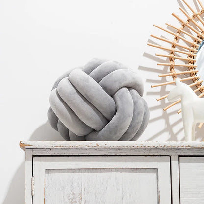 A light grey knot-shaped cushion styled on a sideboard, next to an ornament.