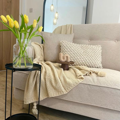 Light grey sofa with decorative pillows, a Nordic waffle blanket and a vase of yellow tulips on a side table.