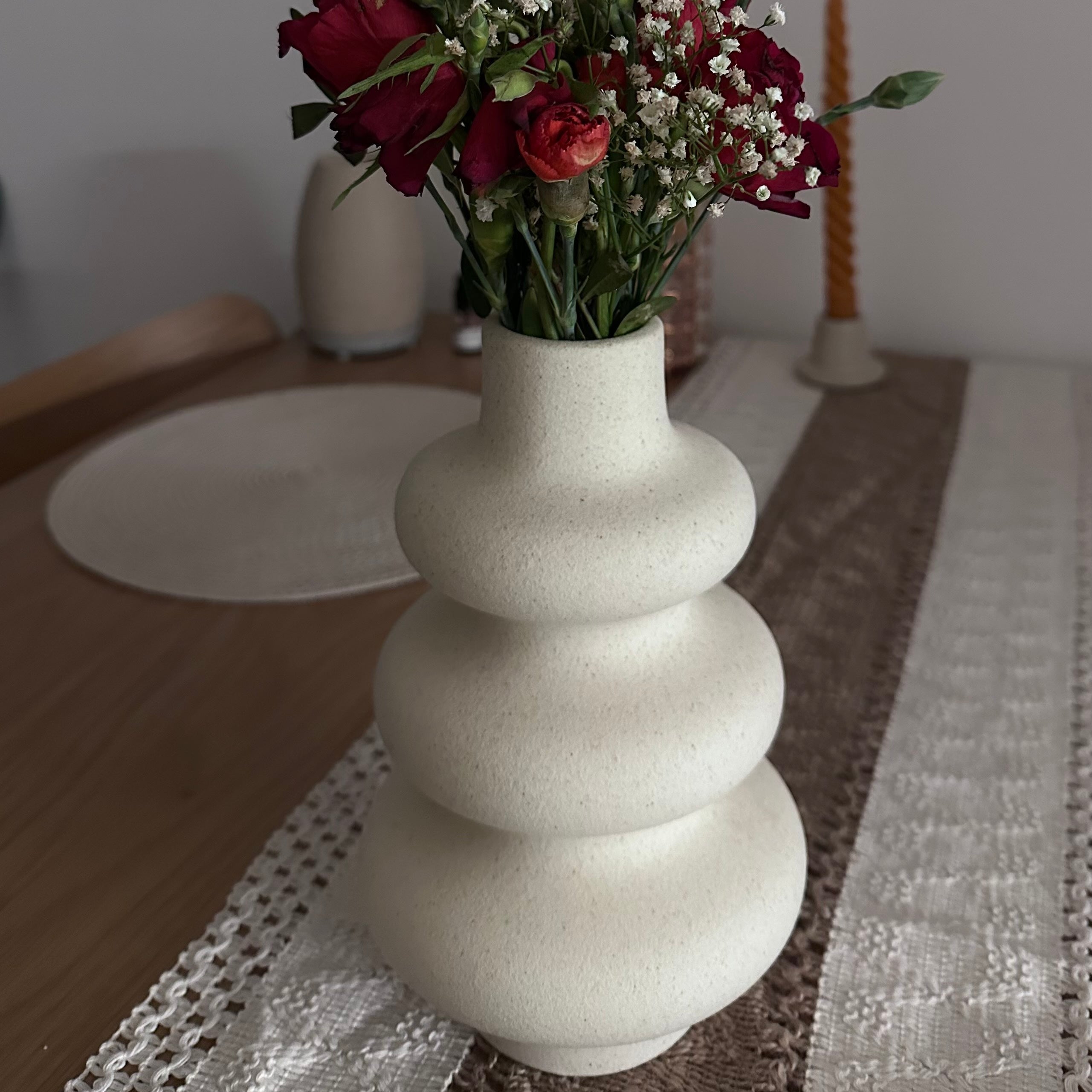 White nordic, wavy textured vase with red flowers on a table