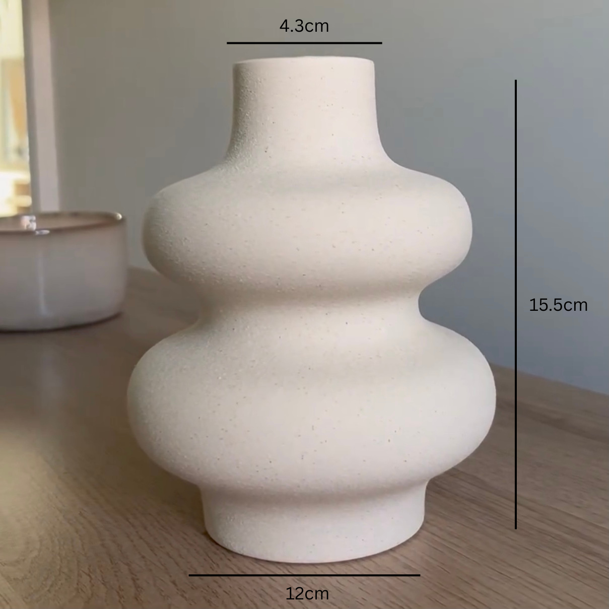 White ceramic, wavy vase on a wooden surface with measurements indicated