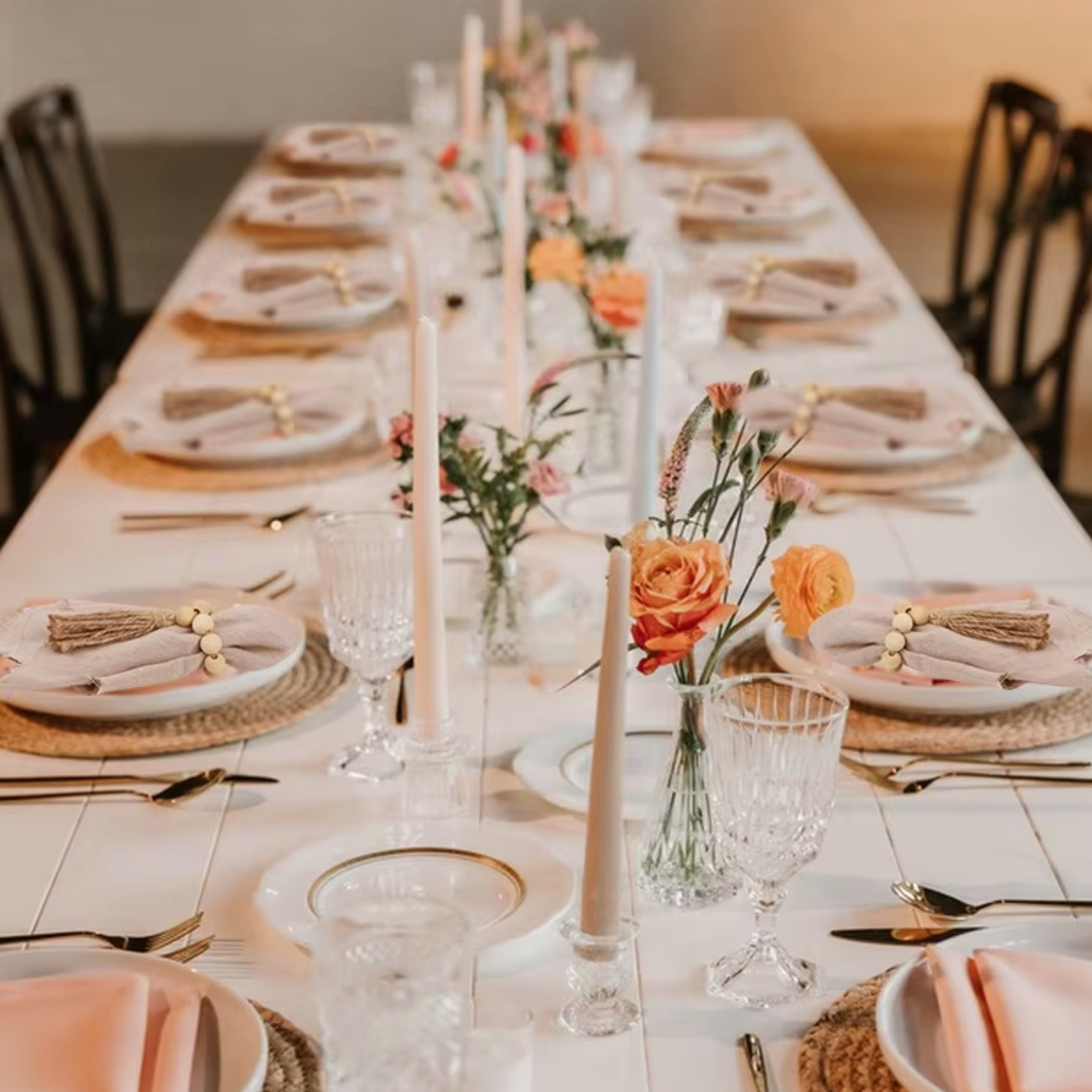 Elegant long dining table set for a meal with floral centerpieces, candles, and neatly arranged plates.