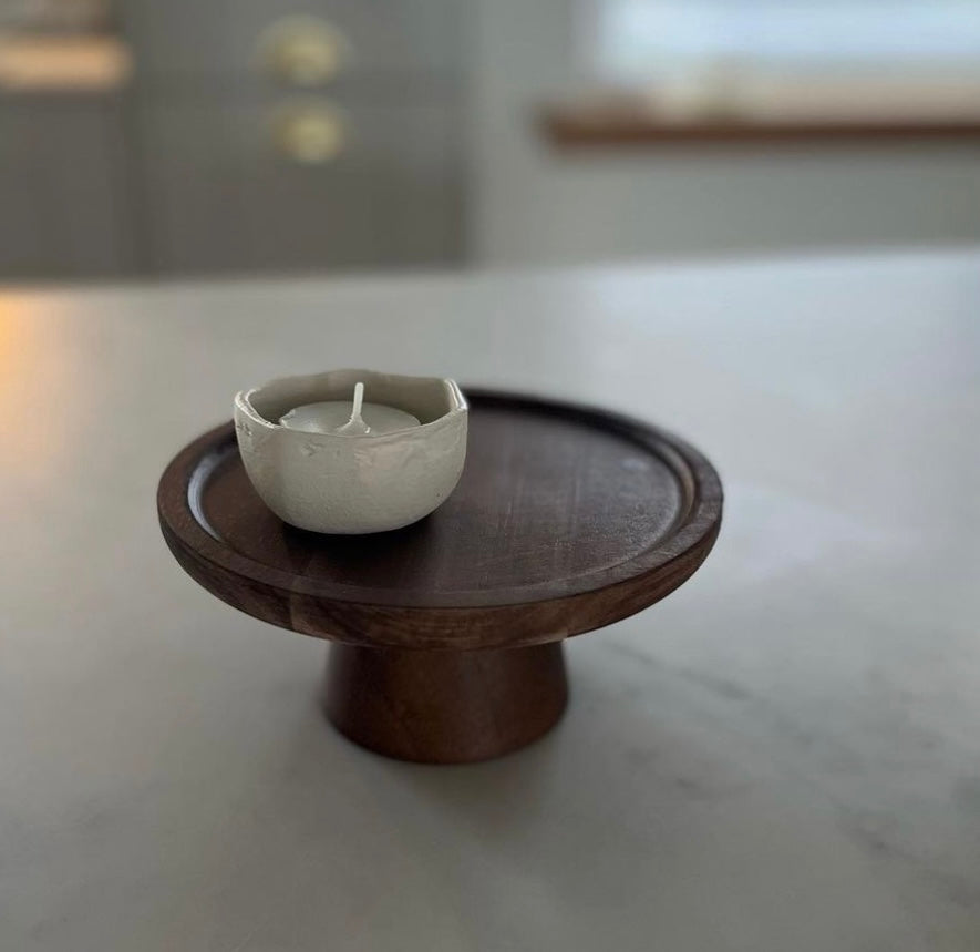 Small natural wooden cake stand with a candle and holder styled on top. 