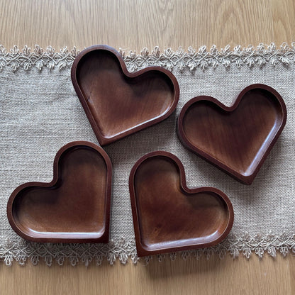 Four heart-shaped wooden trays on a textured fabric surface