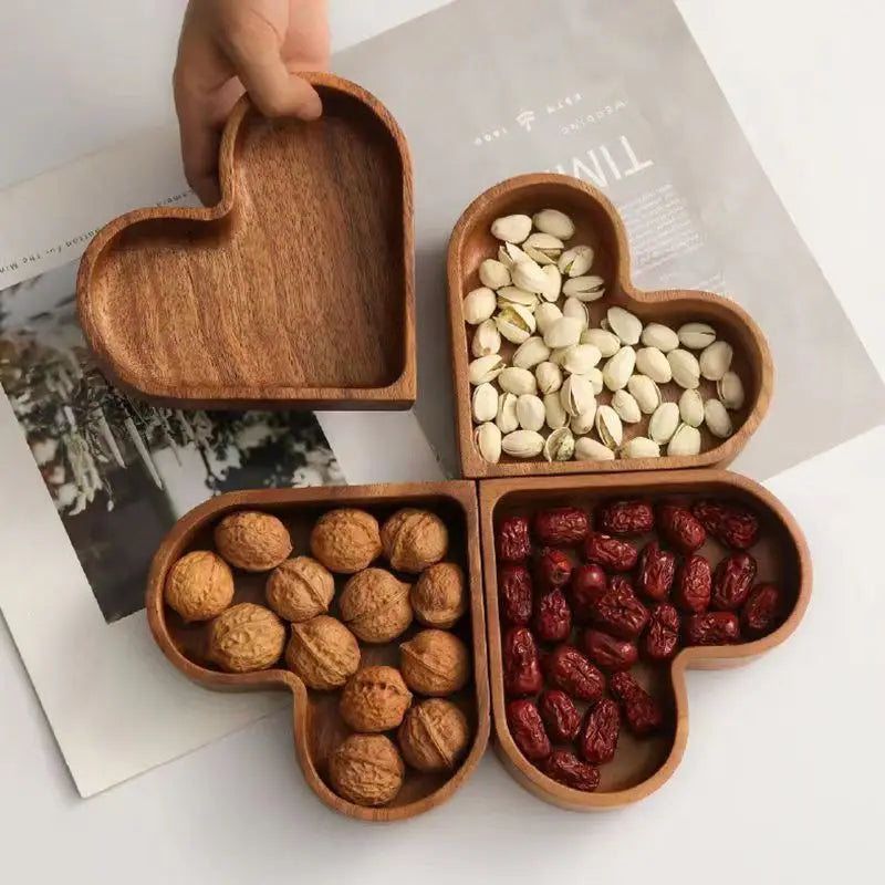 Four heart-shaped wooden trays with compartments filled with nuts and seeds on a magazine background