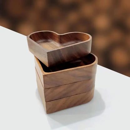 Four wooden heart-shaped food trays, stacked on a white surface with a blurred brown background