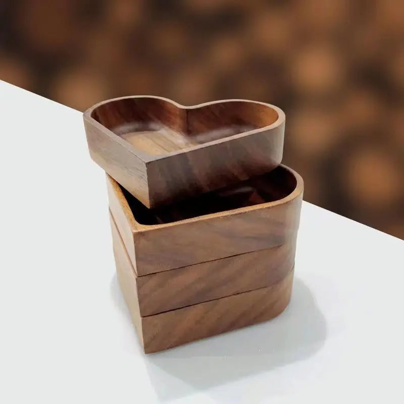 Four wooden heart-shaped food trays, stacked on a white surface with a blurred brown background